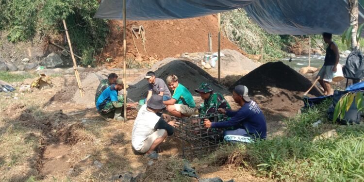 Warga bersama TNI melakukan perakitan besi untuk pondasi cakar ayam sebagai bagian dari pembangunan infrastruktur jembatan